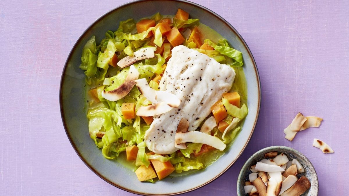 Süßkartoffelcurry mit Kabeljaufilet, Lauch und Kokosraspeln, serviert in einer Keramikschale, garniert mit frischem Pfeffer.