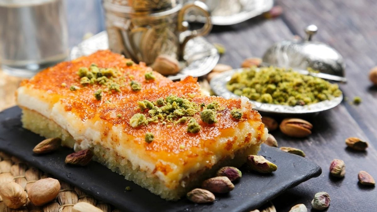 Frontalsicht: zwei flasche kunchenstücke liegen auf einem Untergrund aus Schiefer. die kuchen sind mit Pistaziem berstreut und haben eine feuchte Oberfläche. Auch frumherum liegen viele Pistazien.