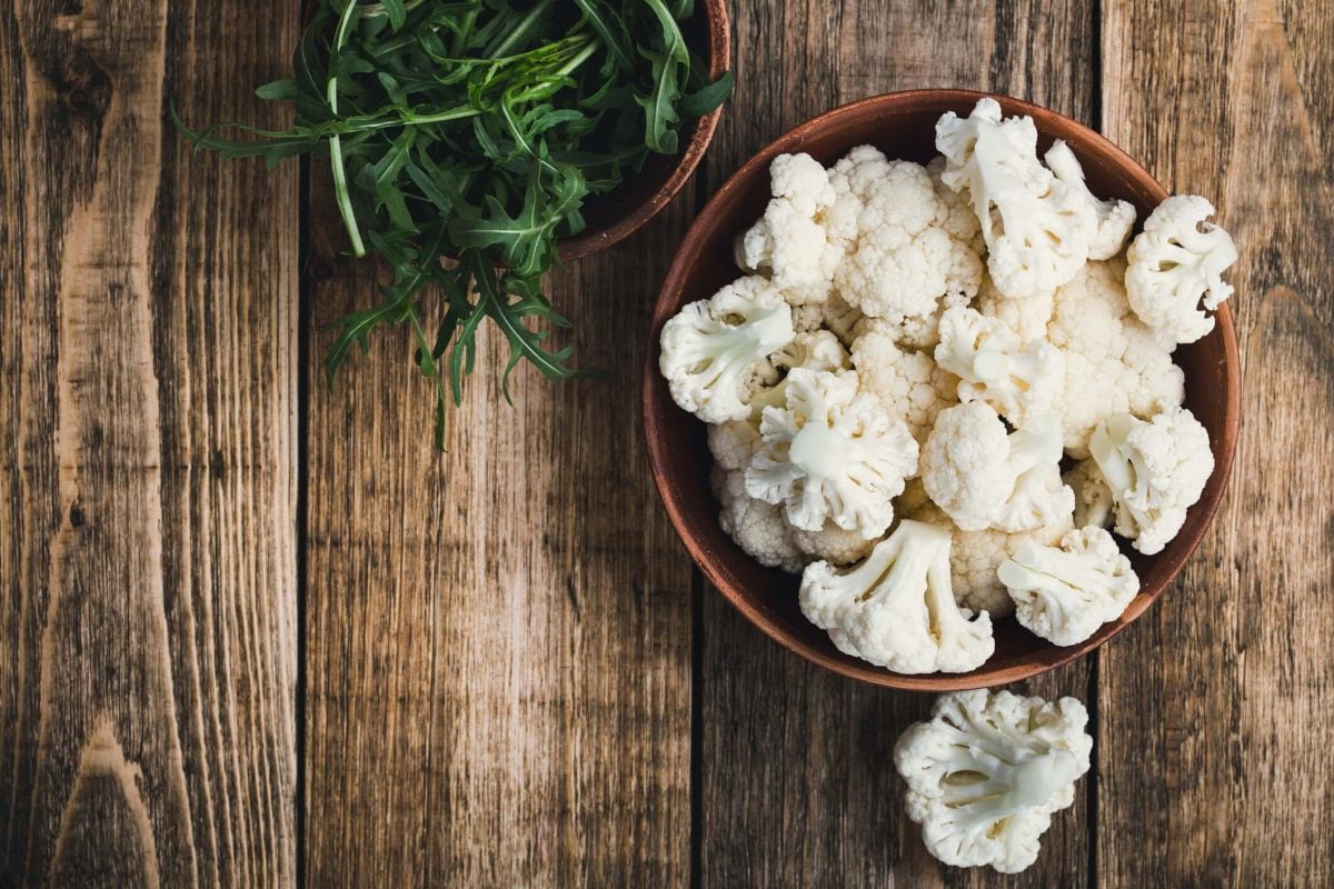Kann man Blumenkohl roh essen? Blumenkohlröschen in einer Holzschale auf Holtisch. Daneben Salat. Draufsicht.