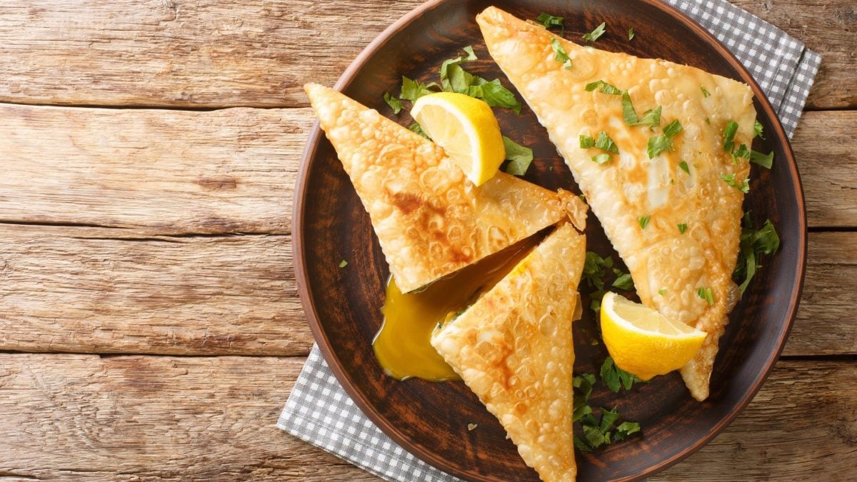 Tunesische Teigtaschen Brik mit Thunfisch und Ei auf braunem Teller mit Zitrone und Petersilie. Draufsicht.