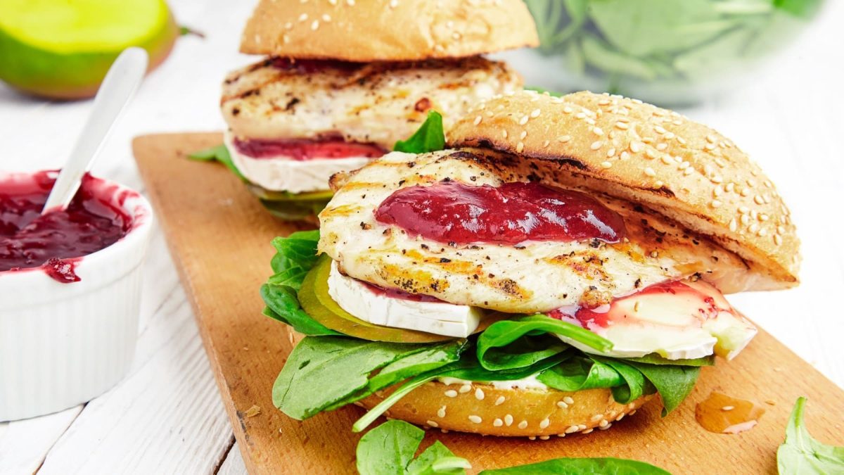 Zwei Hähnchenburger mit Apfel und Camembert auf einem Holzbrett.
