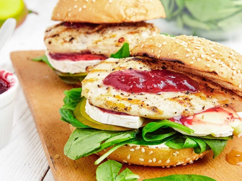 Zwei Hähnchenburger mit Apfel und Camembert auf einem Holzbrett.