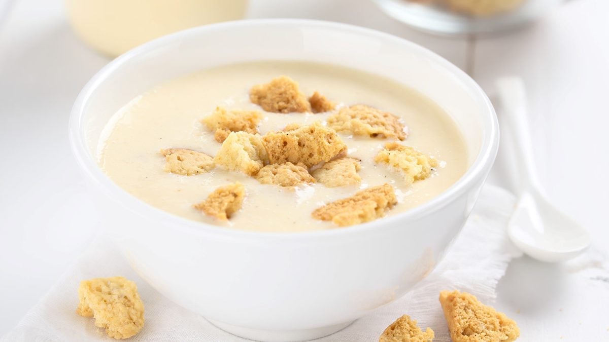 Eine weiße Schale mit der Buttermilch-Mousse auf einem weißen Tisch mit zerbrochenen Keksen.