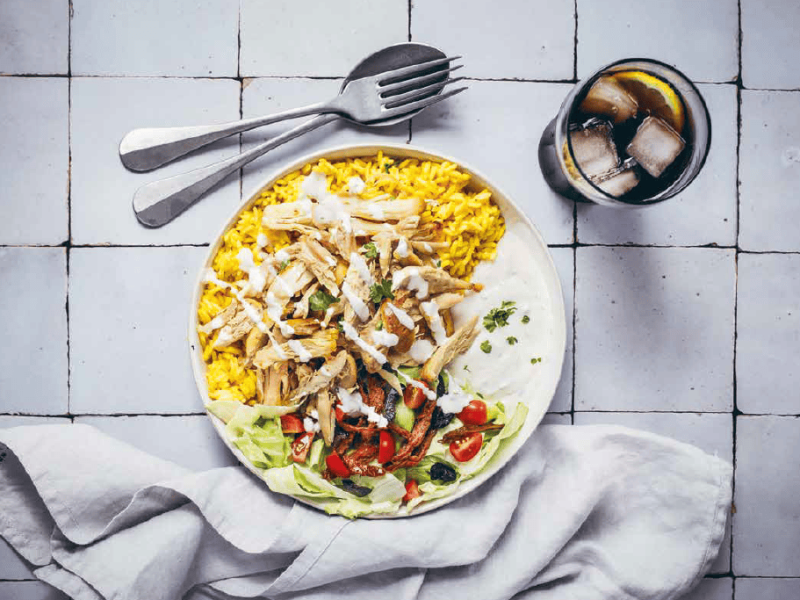 Hühnen, Reis und Salat auf einem Teller in der Draufsicht, daneben ein Glas Cola mit Eis und Besteck. Rezept aus dem Kochbuch "Verliebt in New York".