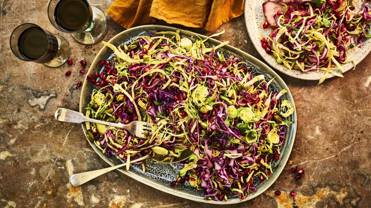Coleslaw mit Pistazien, Granatapfelkernen und Orangen-Sauce, serviert auf einem flachen Servierteller auf einem steinernen Tisch.