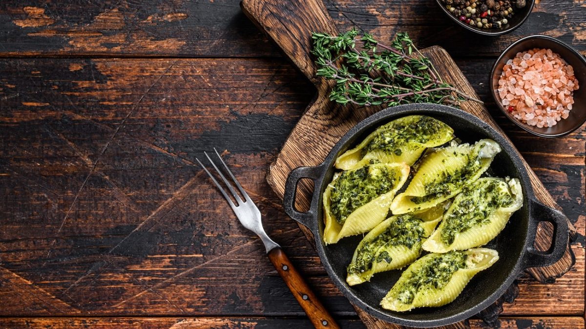 Draufsicht: Eine dunkle Pfanne in der gefüllte Muschelnudeln sind. Die Füllung besteht aus Spinat und Ricotta