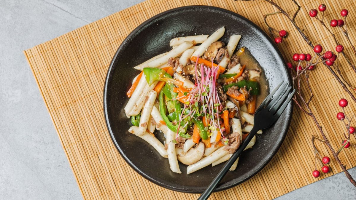 Ein schwarzer Teller mit Gungjung Tteokbokki auf einer Bambusmatte