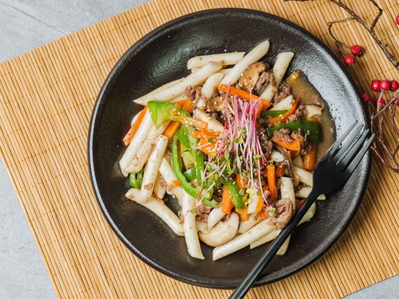 Ein schwarzer Teller mit Gungjung Tteokbokki auf einer Bambusmatte
