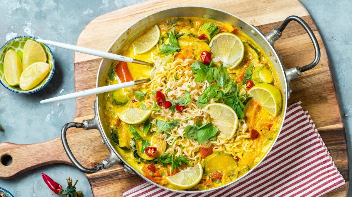 Eine große Schüssel mit Thai-Curry-Nudelsuppe auf einem Holzbrett.