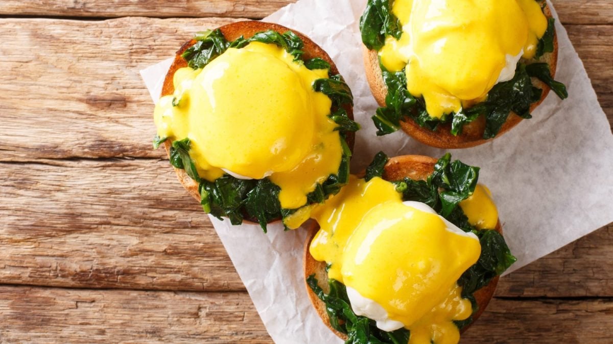 Drei Brötchen mit den Eggs Florentine auf Backpapier und einem dunklen Holztisch von oben fotografiert.