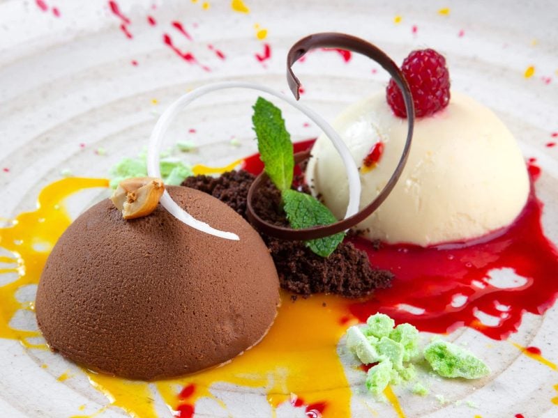 Was sind die Unterschiede zwischen Eis, Parfait und Sorbet? Drei Sorten Eis mit Fruchtsaucen und Schokoladendekoration auf weißem Teller. Draufsicht.