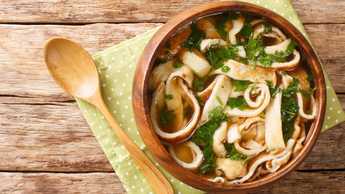 Eine warme braune Schüssel auf einem Holztisch mit der Frittatensuppe.