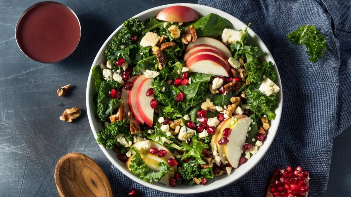 Eine weiße Schale mit dem Grünkohl-Apfel-Salat auf grauem Untergrund von oben fotografiert.