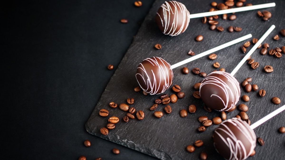 Mehrere Kaffe Cake Pops neben Kaffeebohnen vor schwarzem Hintergrund.