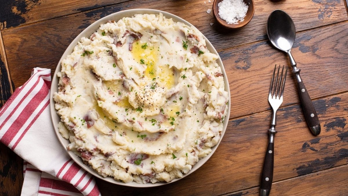 draufsicht ein Knoblauch-Kartoffelpüree ist in einer großen, flachen Schüssel. Drumherum liegen Besteck und ein Küchenhandtuch.