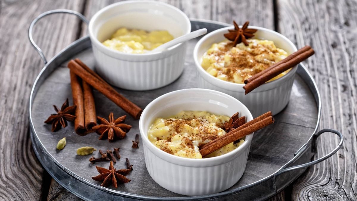 Drei Schalen Lebkuchen-Milchreis mit Zimtstangen, Sternanis und Zimt-Zucker.