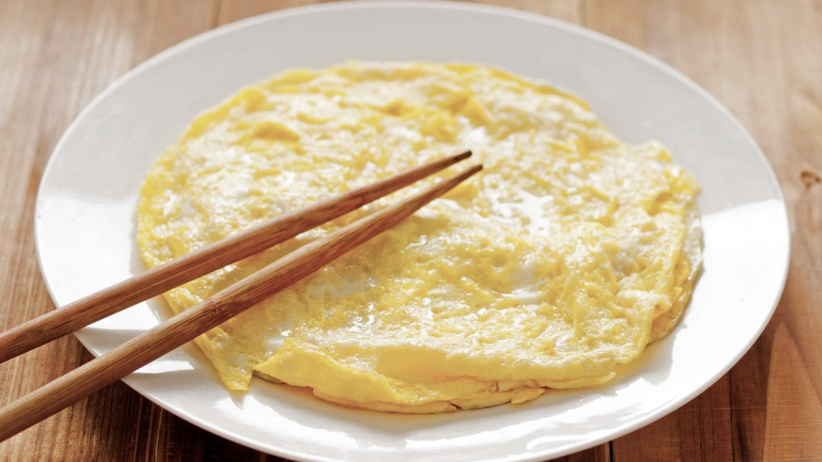 Mini Omeletts auf weißem Teller auf Holztisch mit Essstäbchen. Draufsicht.