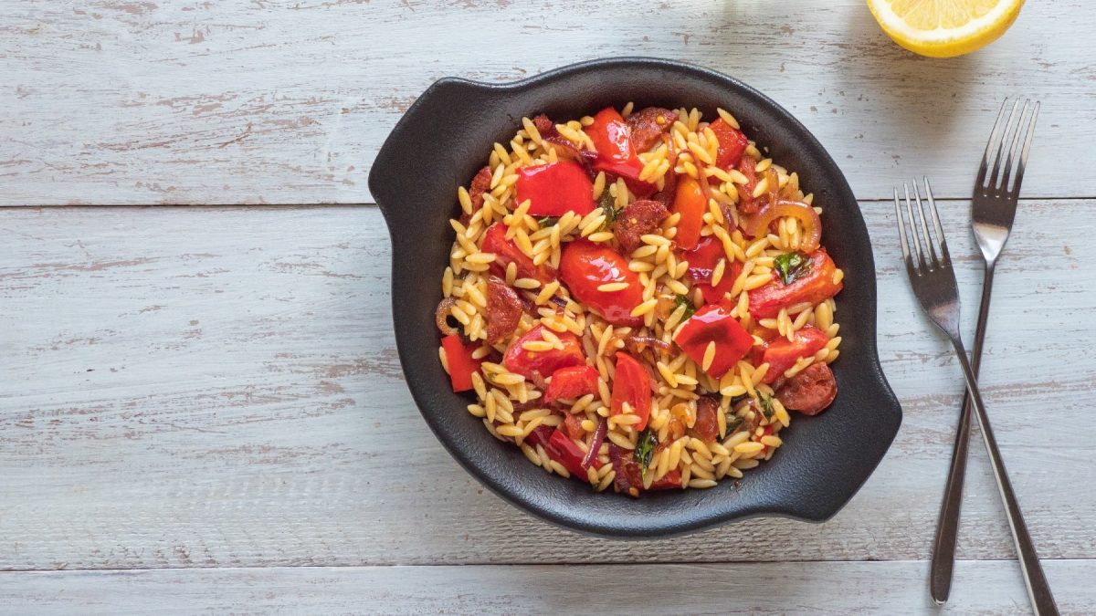 Ein schwarzer Topf mit der Chorizo-Pasta auf einem hellen Holztisch mit zwei Gabeln daneben.