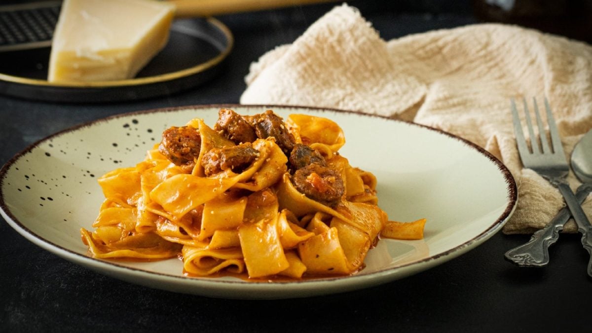 Ein grauer Teller mit der PAsta in roter Sauce und Wurst.