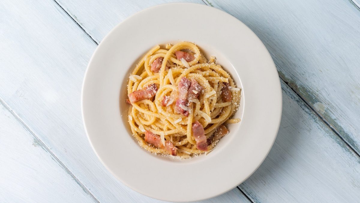 Pasta alla gricia mit Speck und Käse auf weißem Teller.