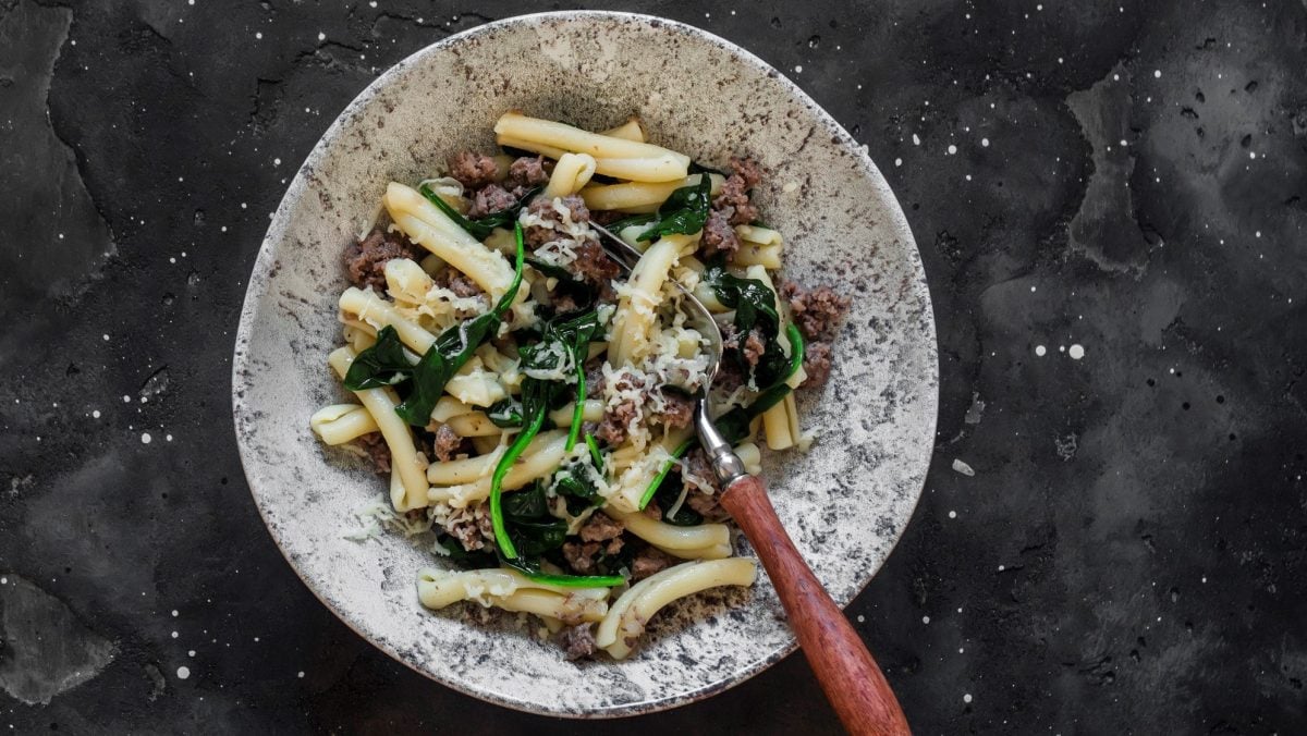 Ein grau-weiß-marmorierter Teller mit der Pasta auf einem dunkelgrauen Untergrund von oben fotografiert.