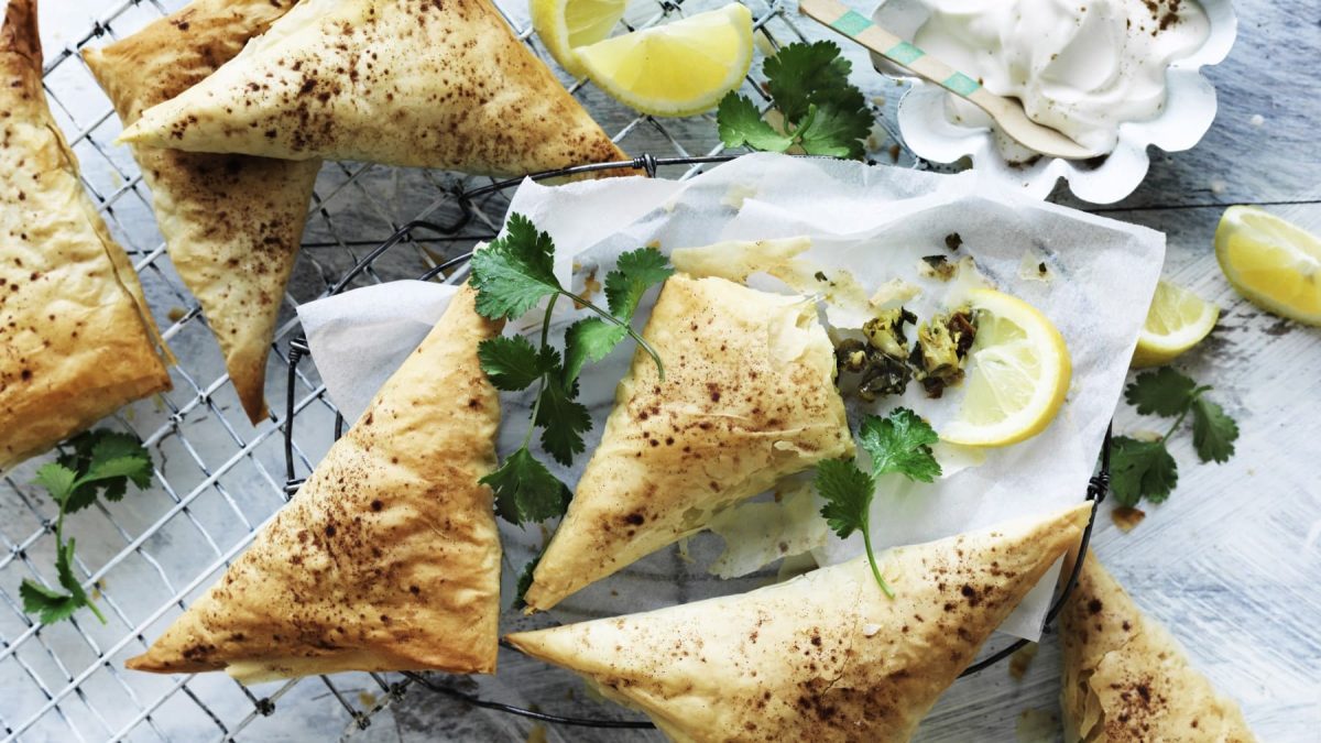 Einige Pastilla-Dreiecke mit Blumenkohl garniert mit Zitrone und Petersilie auf einem Gitter vor hellem Hintergrund.