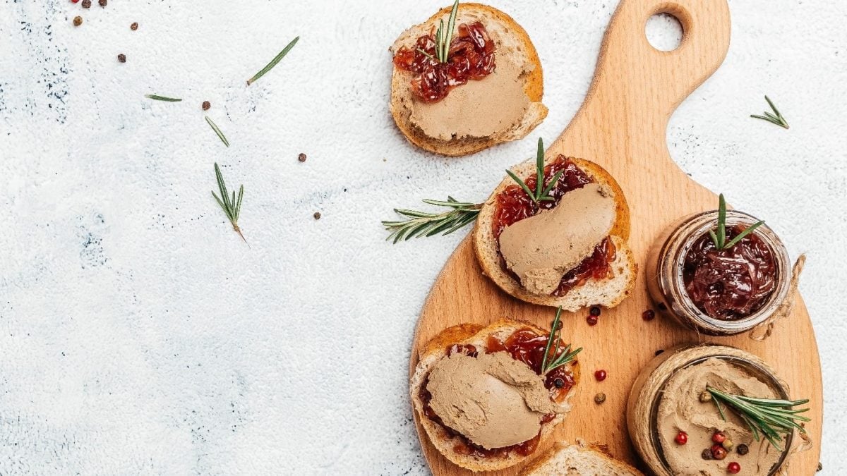 Ein kleines Holzschneidebrett mit einigen belgten Broten und der Zwiebelmarmelade. Garniert mit rotem Pfeffer und Rosmarin.