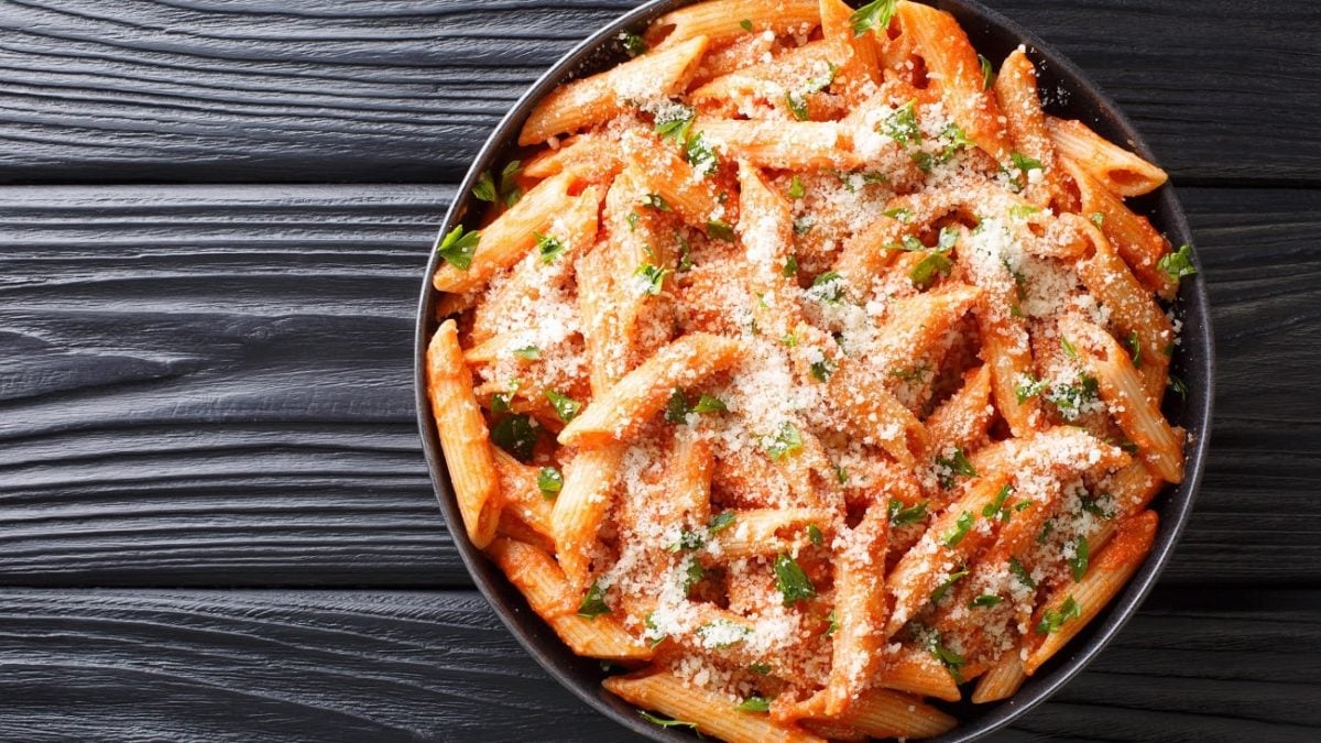 Draufsicht: auf einem dunklen Untergrund liegt ein dunkler teller. auf dem ist ein nudelgericht mit tomatensauce.