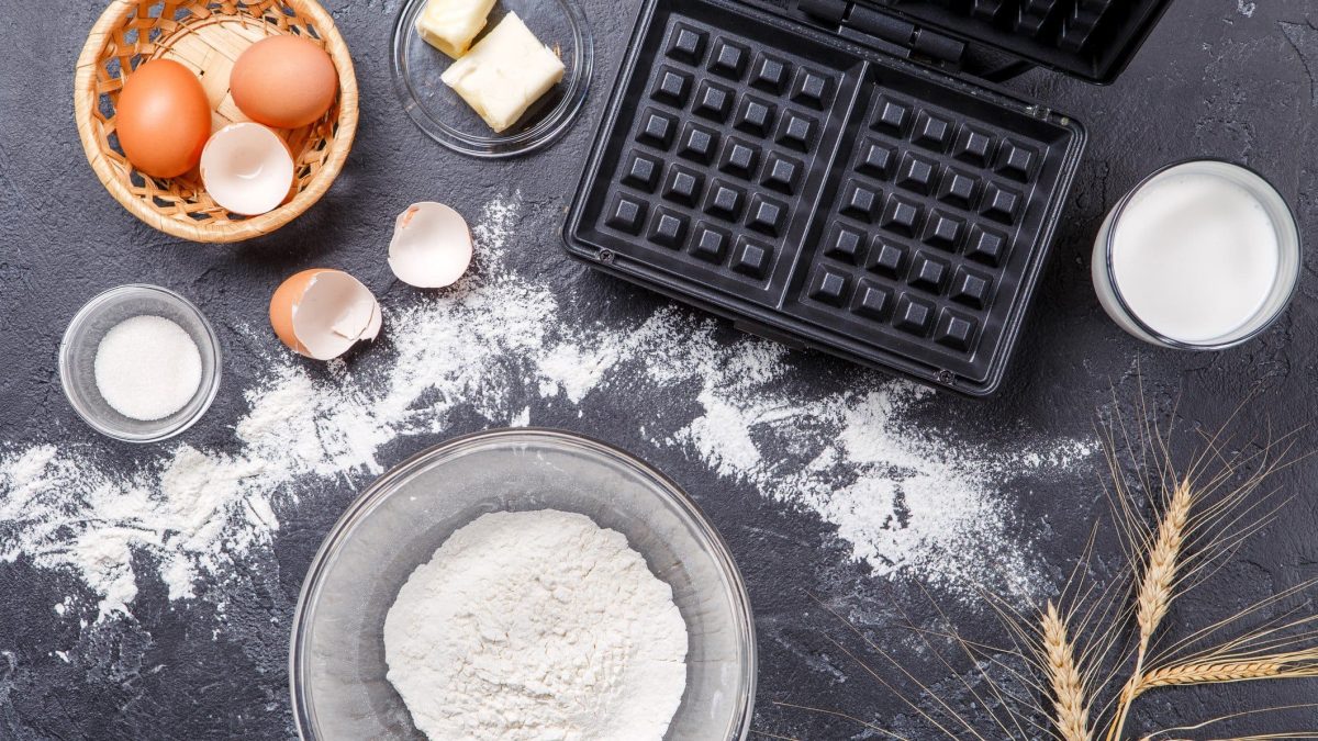 Eine Arbeitsfläche mit allen zutaten für die Plätzchen udn einem leeren aufgeklapptem Waffeleisen.