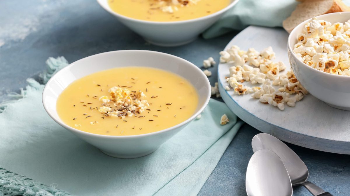 Zwei weiße Schalen mit der Popcorn-Suppe auf einem blauen Tischtuch. udn einer großen Schale mit Popcorn.