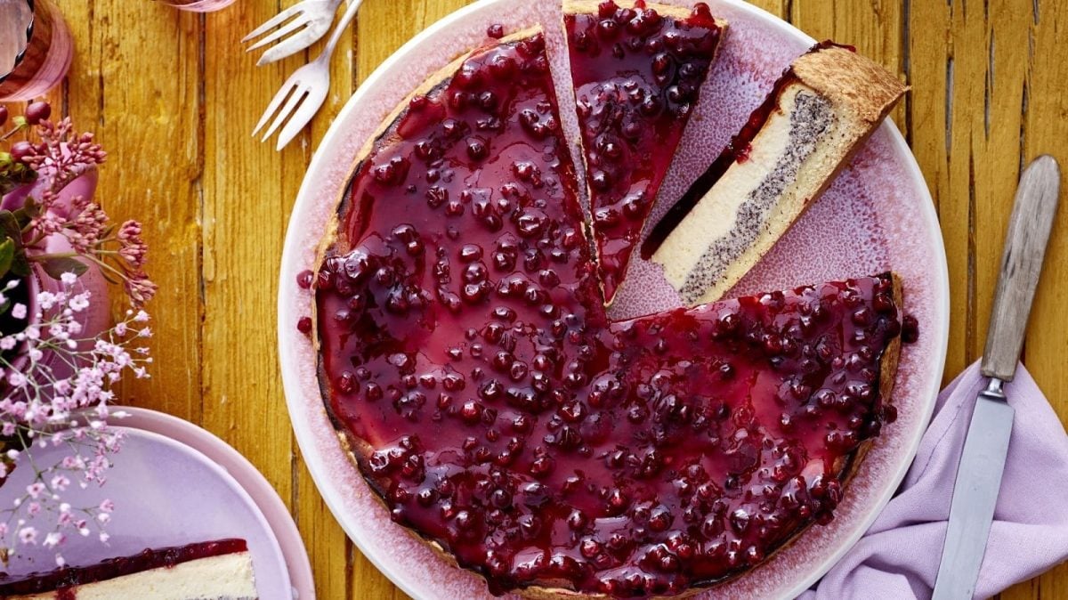 Draufsicht: Angeschnittener Preiselbeer-Mohn-Käsekuchen auf einem rosa Teller.