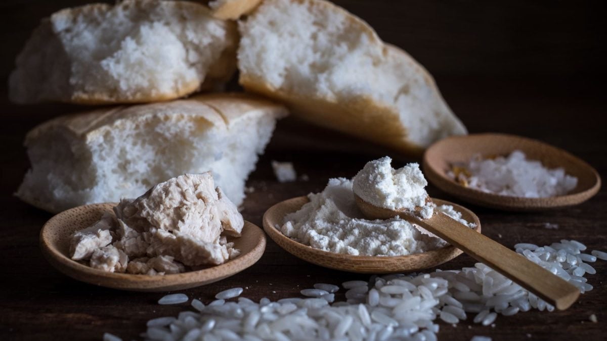 Das Reisbrot im Hintergrund. Im Vordergrund drei kleine Holzschippen mit Reismehl, Hefe und körnigem Reis.