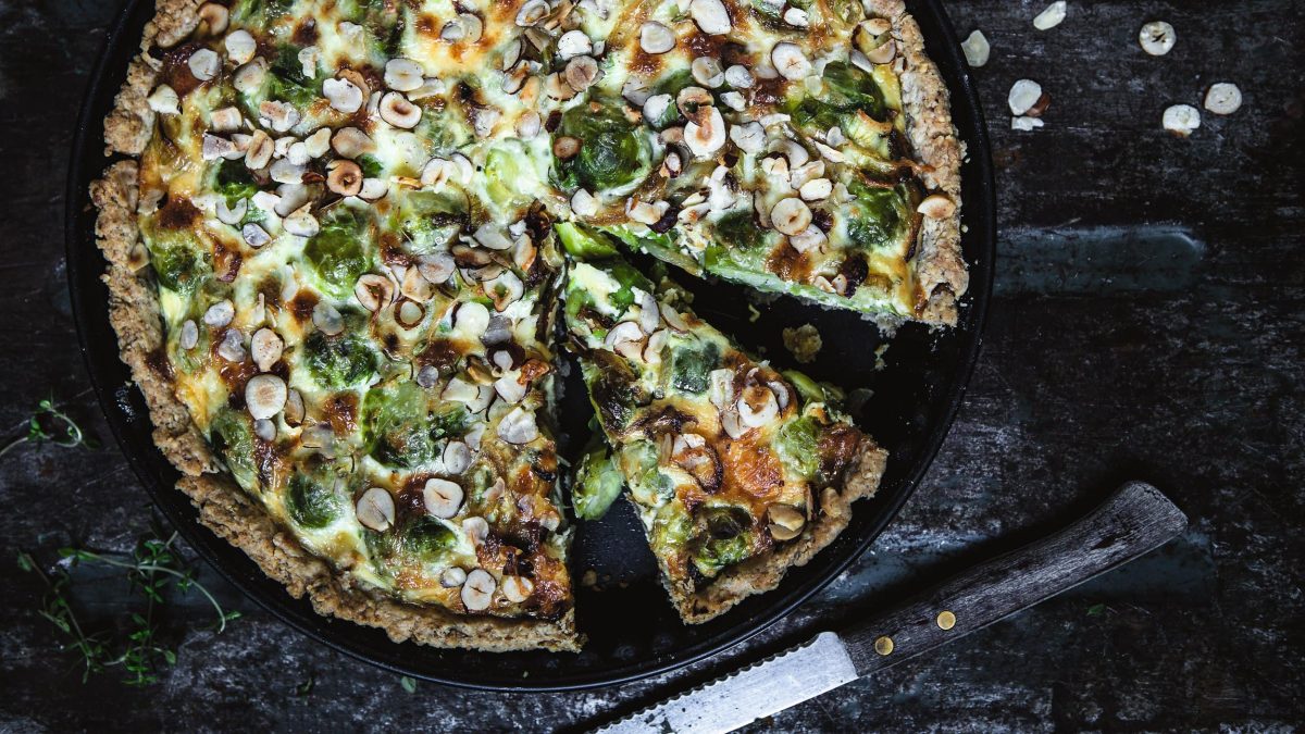 Eine angeschnittene Rosenkohl-Haselnuss-Tarte in der Draufsicht, daneben ein Messer.