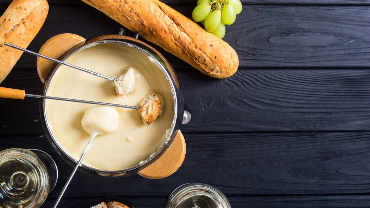 Ein Topf schnelles veganes Käsefondue mit Spießen, Weintrauben und Baguette in der Draufsicht.