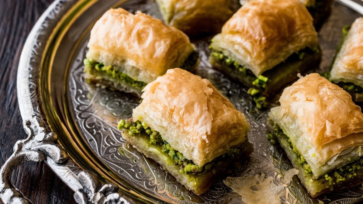 Baklava mit Pistazienfüllung auf einem silbernen Tablett vor dunklem Hintergrund.