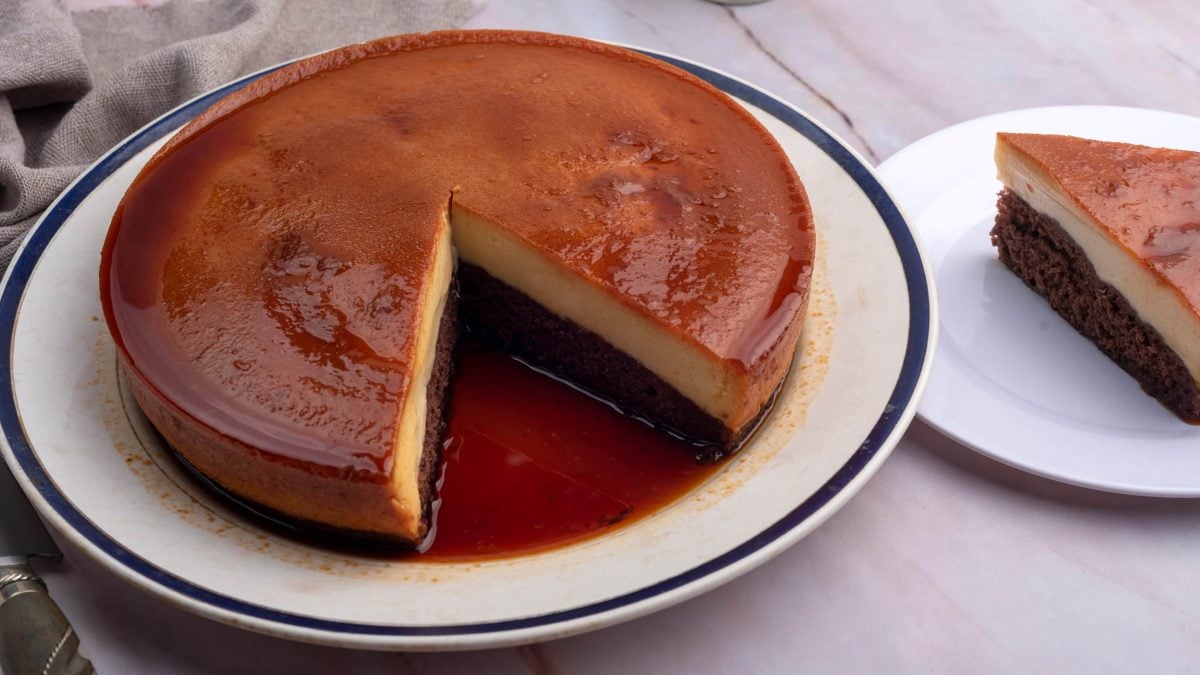 Umgedrehter Schokoladenkuchen mit Milchmädchen-Flan und Karamell auf weißem Teller auf weißem Untergrund. Daneben ein Stück Kuchen auf Kuchenteller. Draufsicht.