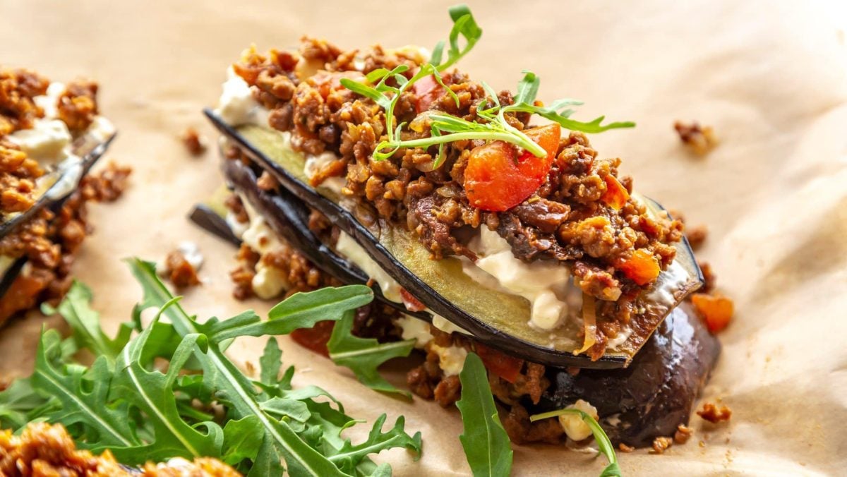 Ein Stück vegane Auberginen-Lasagne mit Linsen-Bolognese und Ruccola.