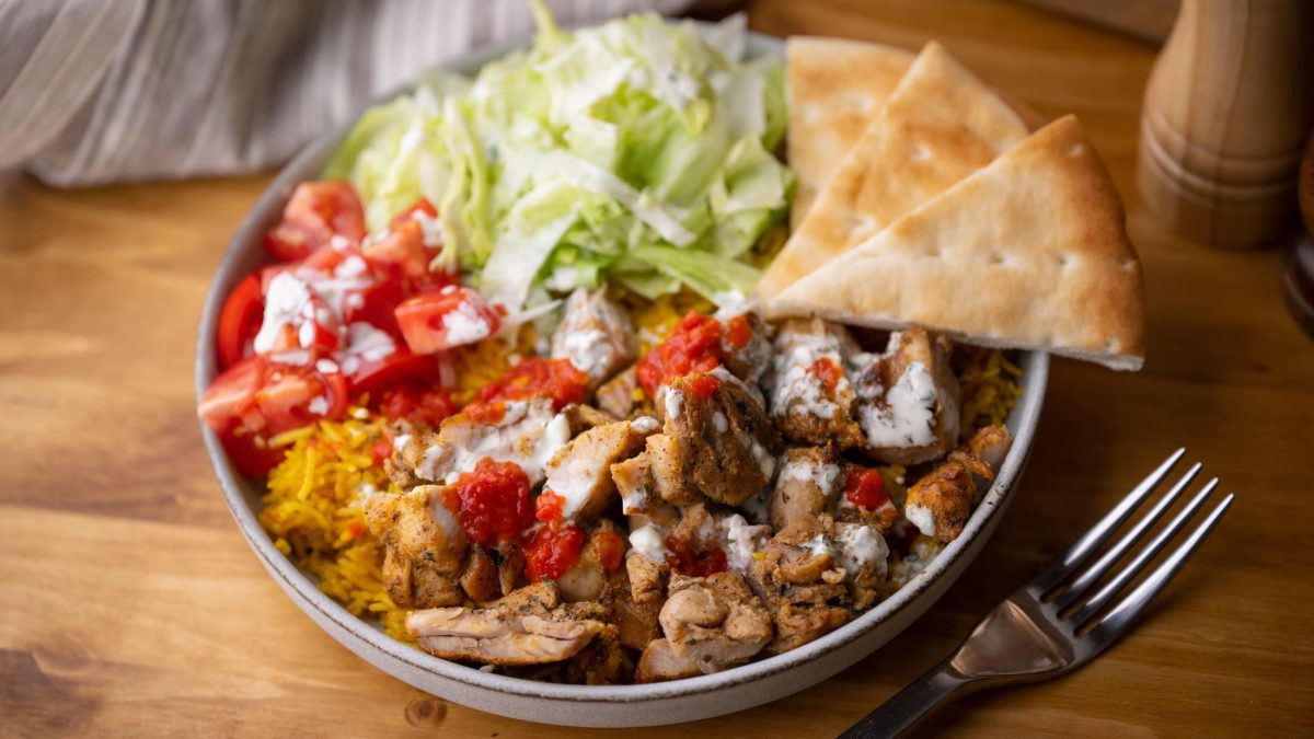 Eine vegane Gyros-Bowl mit Salat, Tomaten, Reis und veganem Gyros, daneben Pitabrotscheiben.