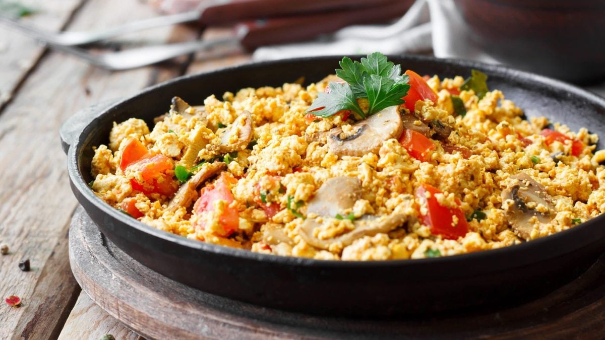 Eine gusseiserne Pfanne, darin veganes Rührei mit Chili-Pilzen und Tomaten sowie Petersilie.