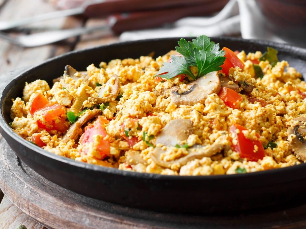 Eine gusseiserne Pfanne, darin veganes Rührei mit Chili-Pilzen und Tomaten sowie Petersilie.