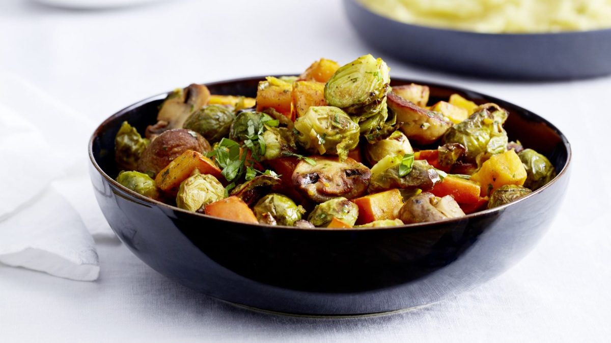Warmer Röstgemüse-Salat in einer schwarzen Schüssel vor hellem Hintergrund.