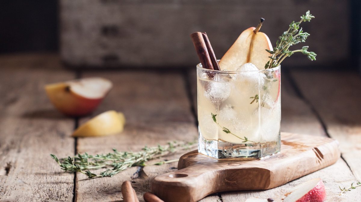 Ein Glas winterlicher Gin Tonic mit Birnensaft und Zimt, Eiswürfeln und Thymian.