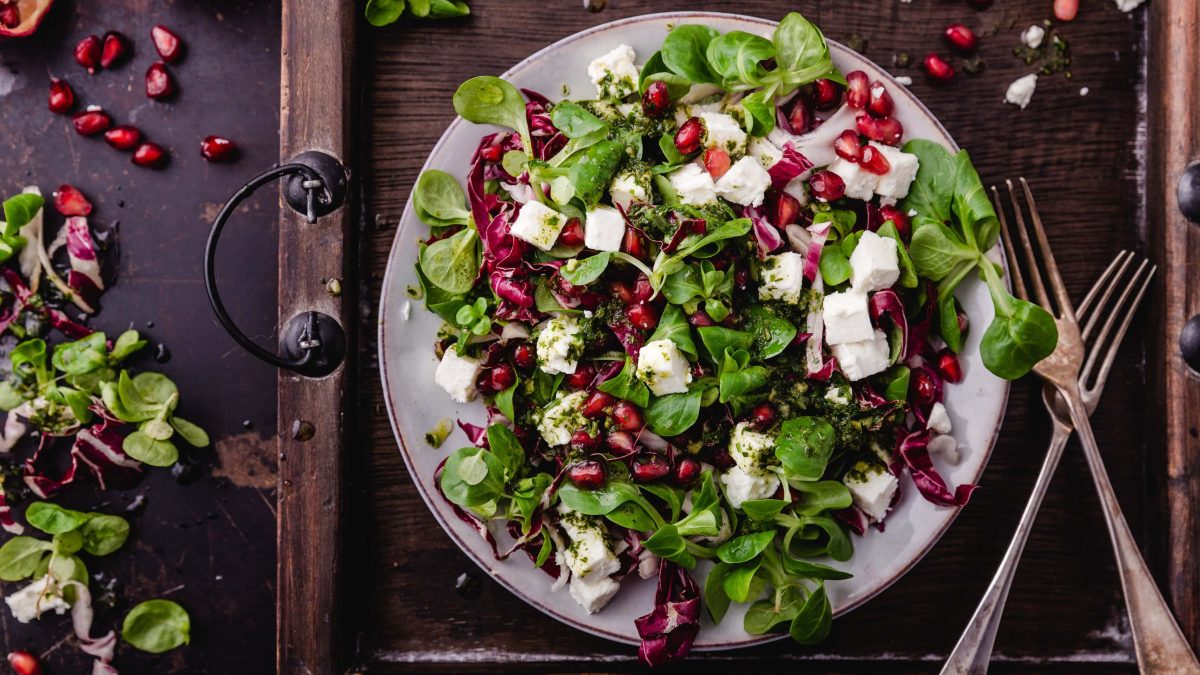 Draufsicht: Eine Wintersalat mit Radicchio, Feta und Granatapfel steht auf einem Tablettt. Daneben liegen zwei Gabeln aus Metall.