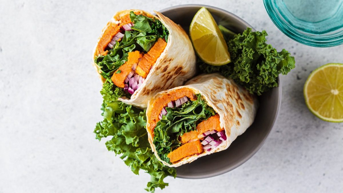Wraps mit Süßkartoffeln und Grünkohl, zusammen mit Zwiebeln eingewickelt und halbiert serviert mit frischer Zitrone.