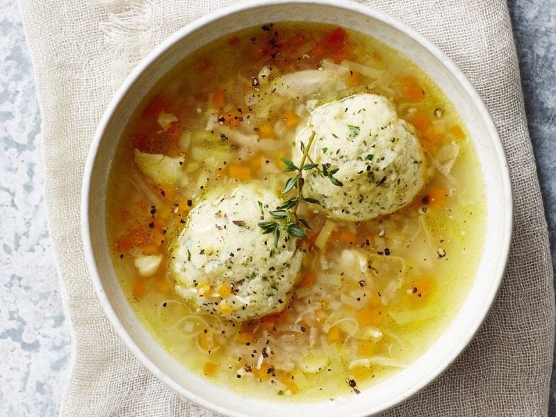 Draufsicht: eine weiße Schüssel mit einer klaren Suppe in der zwei Knödel sind.
