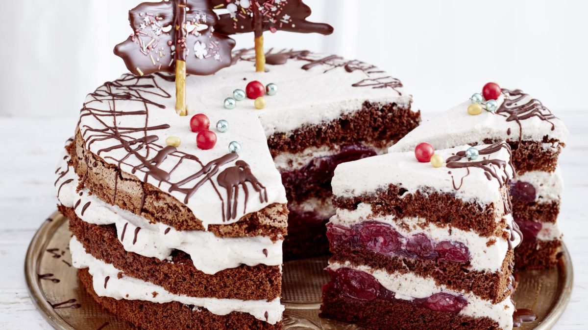 Auf einem Teller liegt eine Schwarzwälder Glühwein-Kirschtorte. Sie ist mit Salzstangen und Zuckerperlen dekoriert.
