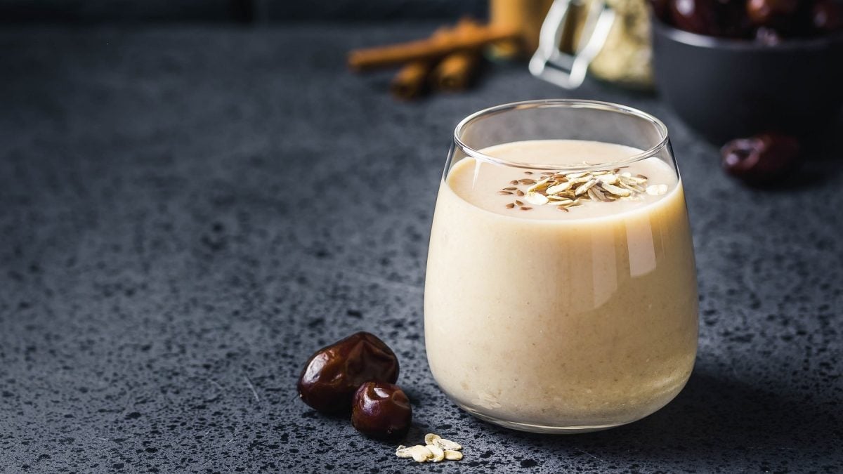 Ein Glas mit dem Bananen-Mate-Smoothie auf einem dunkelblauem Untergrund mit Datteln.