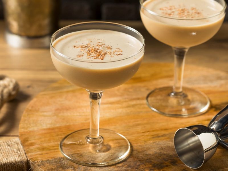 Ein Holztisch mit zwei Gläsern, gefüllt mit dem Cocktail Brandy Alexander.