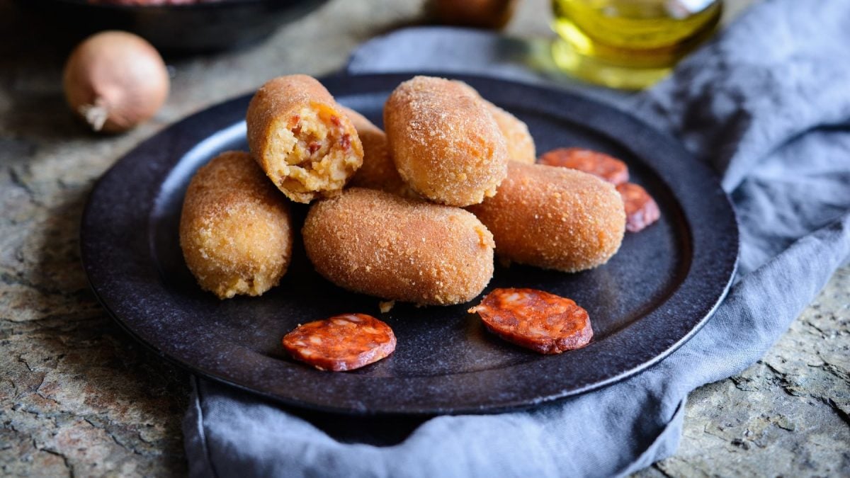Ein dunkler Teller mit den Chorizo-Kroketten auf einem grauen Marmoruntergrund mit blauem Tuch.