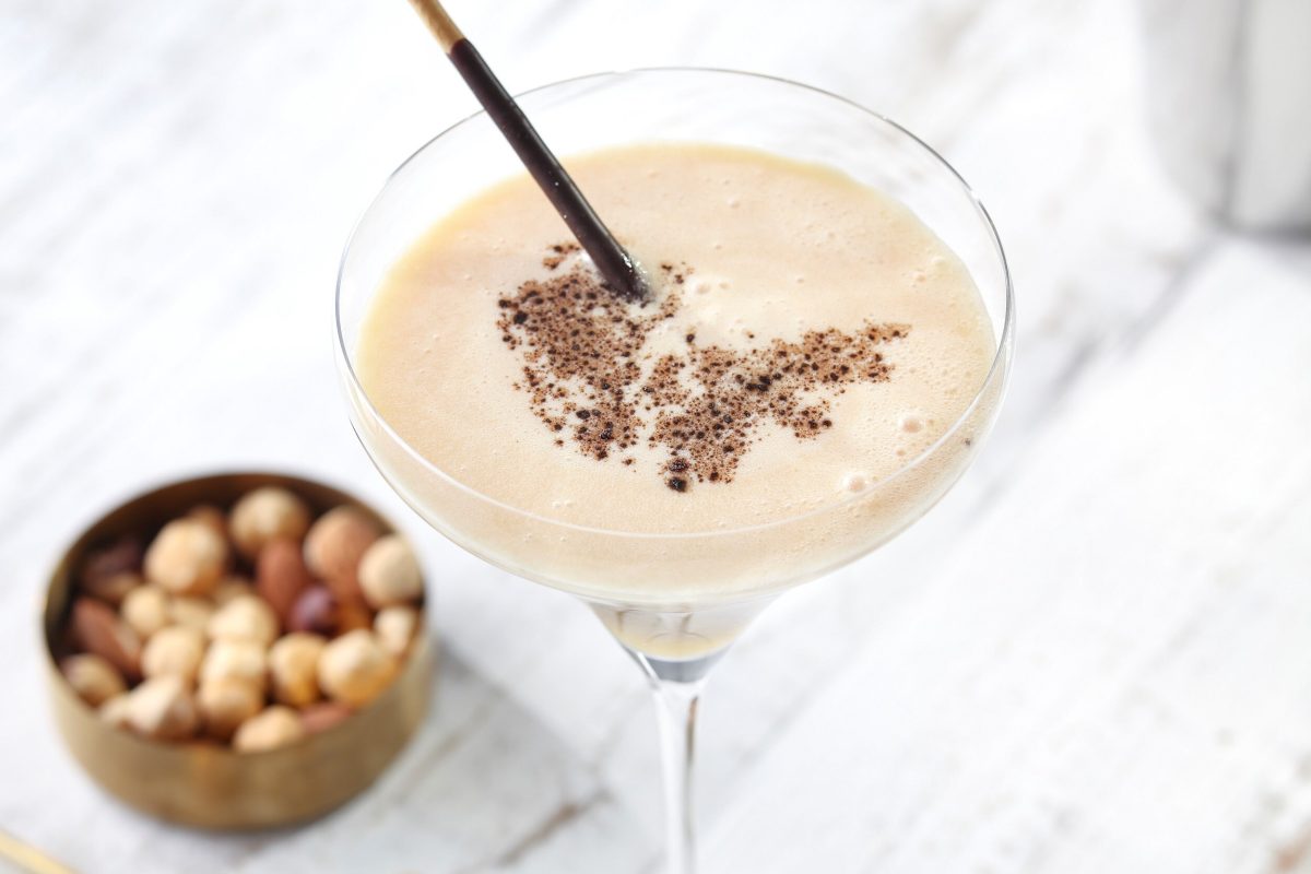 Ein weißer Cocktail im Martiniglas aus dem Buch "Cocktails – die besten Drinks", daneben unscharf eine Schale Nüsse.